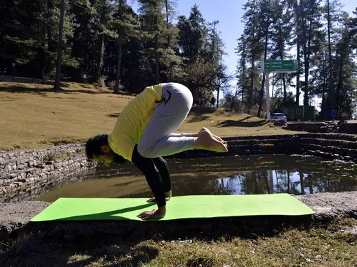 A coach holding crow pose beside a pond in the Himachal hills