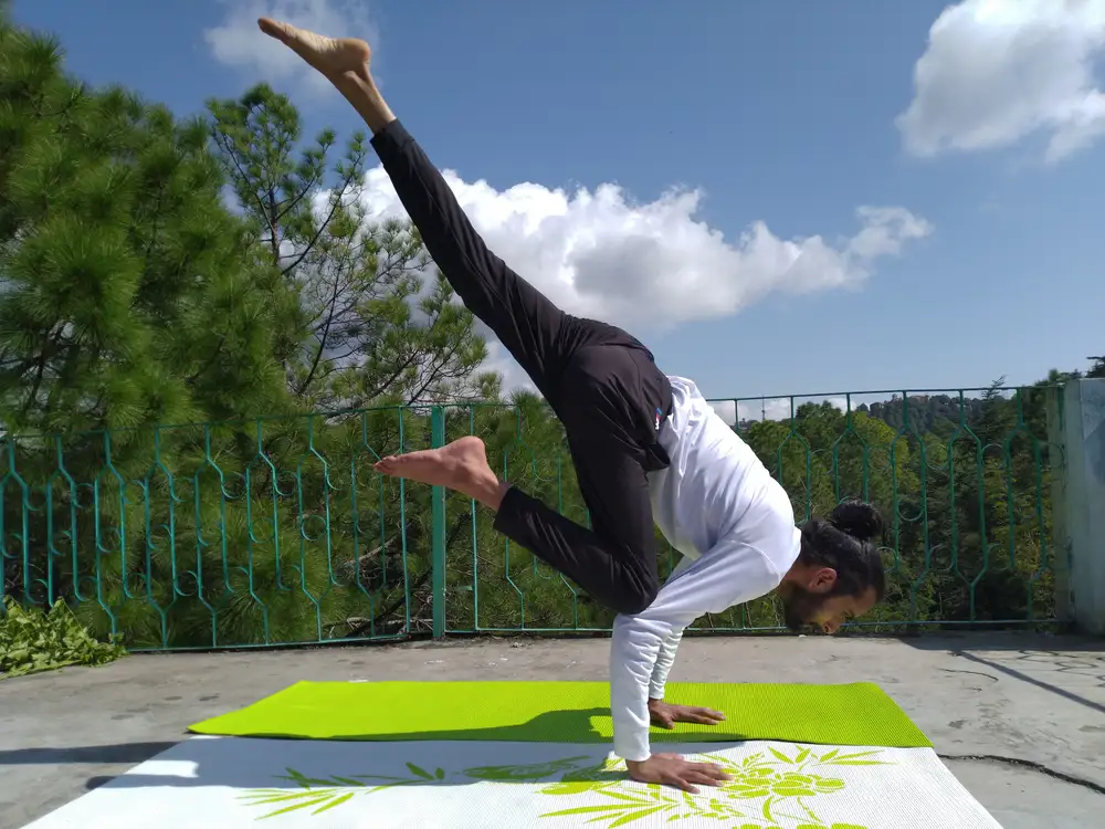 Umesh Yogi holding an arm balance on a terrace above Shimla's pine forest
