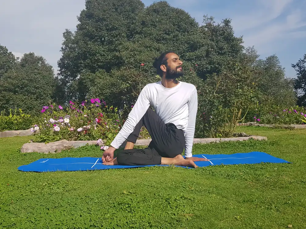 A seated spinal twist practised on a blue mat in a flowering Shimla garden