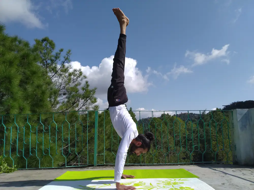 Umesh Yogi in a handstand against blue sky and Himalayan pines