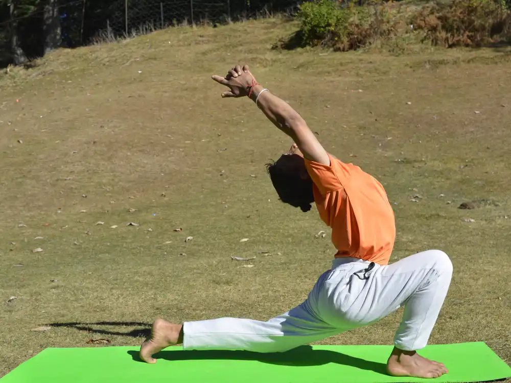 A low crescent lunge with arms extended, practised on open hillside grass