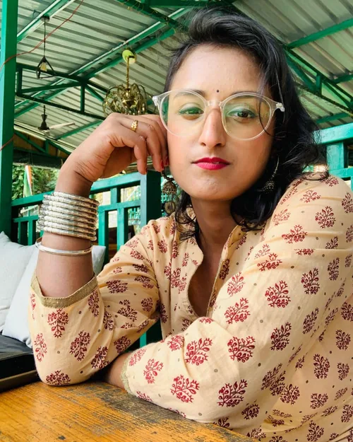 Pragya Mittal, embodiment facilitator, seated at a wooden table under a green pergola